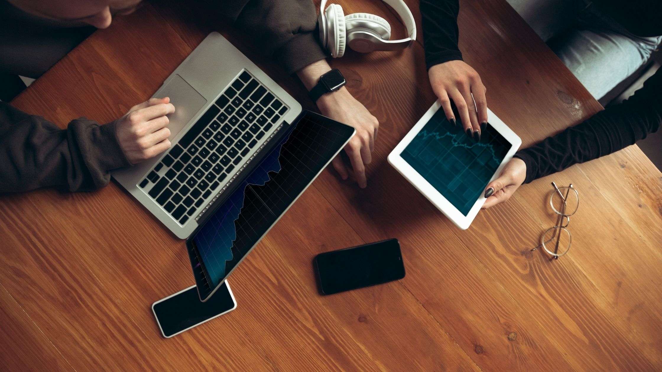 A birds eye view of one person viewing a laptop and another viewing a tablet that shares the same graph chart